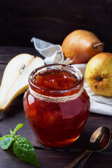 Homemade pear jam in a jar and fresh pears on a wooden background.