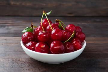 Ripe fresh cherry berries in a plate, dark rustic wooden background. Copy space.