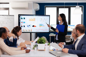 Young team leader in big corporation briefing coworkers pointing at graph meeting. Corporate staff...