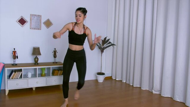 Attractive Indian sportswoman demonstrating Zumba exercises in her fitness studio. Young female trainer energetically doing Zumba dance workout on her favorite music/songs - healthy lifestyle concept