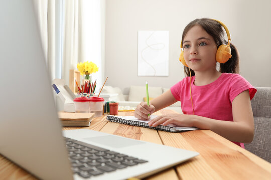Little girl with headphones drawing on paper at online lesson indoors. Distance learning - Powered by Adobe