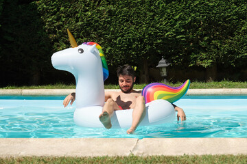 Young happy man on a big unicorn inflatable ring in a swimming pool. Summer concept. © Ladanifer