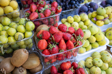 Lots of fresh berries and fruits on the counter at the farmers market. Red strawberries, kiwi and yellow figs.