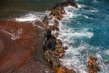 Ocean waves crashing on the rocky island coast. Splashing ocean waves and stones. Red Sand Beach, Maui in in Hawaiian. - Powered by Adobe