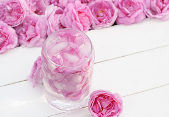 Cold drink made from light pink tea rose petals in a glass glass on white wooden boards with rose flowers