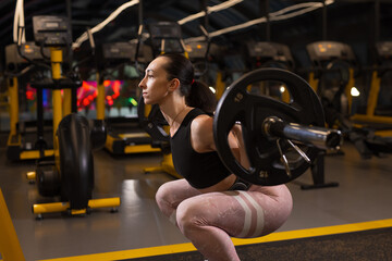 Woman squats with heavy weight on barbell in a gym