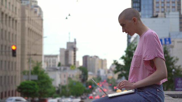 Busy bald woman using laptop computer, typing on keyboard outdoors. Copywriter working online sitting at workplace . High quality 4k footage