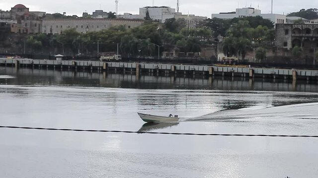 zona colonial, rep&uacute;blica dominicana - 12 de junio de 2021 - peque&ntilde;a embarcaci&oacute;n cruzando el canal del r&iacute;o ozama, ciudad colonial al fondo