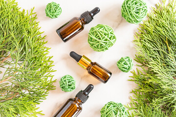 Glass dropper bottles with cosmetic oil, essential or serum on marble background with thuja branches and ratang balls. Concept of natural organic cosmetics. Herbal homeopathic products.