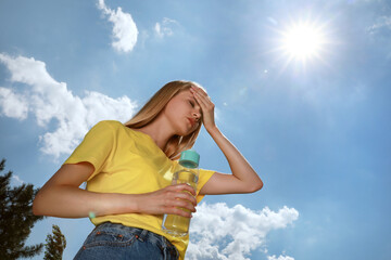 Woman with bottle of water suffering from heat stroke outdoors