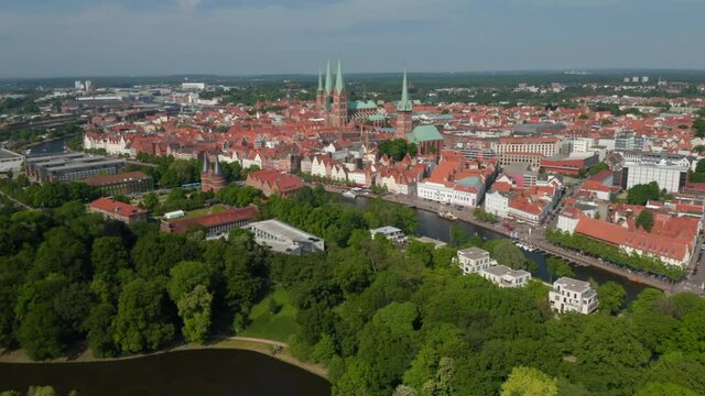 Backwards reveal of green park on island near historic city centre. Aerial panoramic view of town. Luebeck, Schleswig-Holstein, Germany