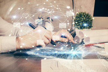 Double exposure of man's hands holding and using a digital device and envelop hologram drawing. E-mail concept.