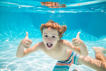 Happy kid boy swim and dive underwater, kid with thumbs up in swimpool. Active healthy lifestyle,...