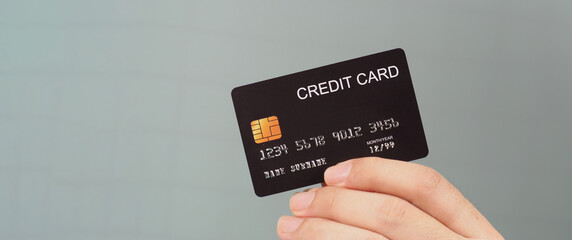 Hand is holding black credit card isolated on grey background.
