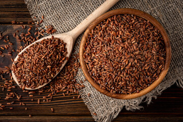 Brown rice in wooden bowl on dark wooden background.