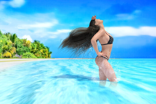 綺麗な青い南国の海にビキニ姿で髪をなびかせて空を見上げる女性