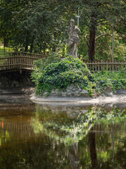 Fototapeta na wymiar Statue of Poseidon with reflection immersed in Nature and Vegetation in front of a Small Lake