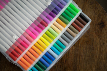 60 pieces of colorful markers in transparent plastic packaging on a wooden background.