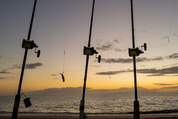 Fishing rod and reel on sea, vacation on blue ocean and summer sunset sky.