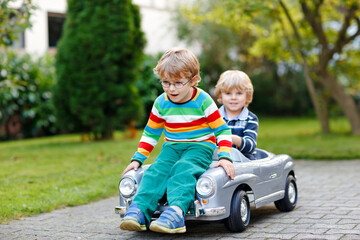Two little preschool boys playing with big old toy car in summer garden, outdoors. Happy children...