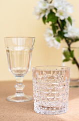 two empty transparent glasses for wine or other alcoholic drinks on a beige background, minimalistic still life of vintage medieval crystal goblets and white flowers, romantic pastel banquet design