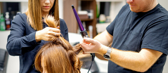 Two hairstylists using a curling iron on customers long brown hair in a beauty salon