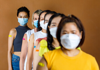 Diversity group of female from multinational ethnic patients wears face mask stand in line by height order look at camera showing colorful plasters on shoulder together after vaccination - obrazy, fototapety, plakaty