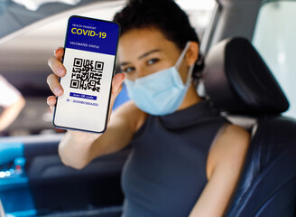 Woman in car wears face mask show screen of smartphone with Covid-19 or coronavirus health passport vaccinated status and QR code sign to show she already get vaccine. Herd immunity concept