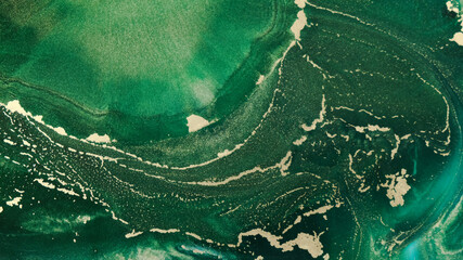 Close-up emerald ink with gold waves spread like an ocea, top view. Abstract fluid art. Goldish...