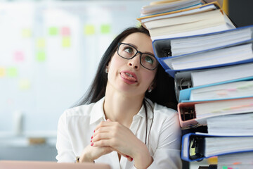 Tired young woman sitting at desk with lot of documents closeup