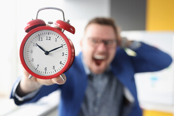 Screaming businessman holds red alarm clock in hands