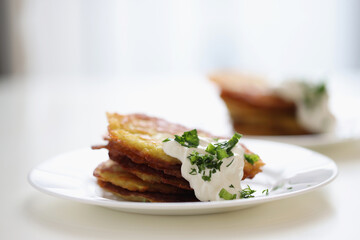 Potato pancakes with sour cream and herbs on white plate closeup