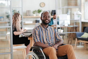 Portrait of African young businessman sitting on wheelchair and smiling at camera while working at...