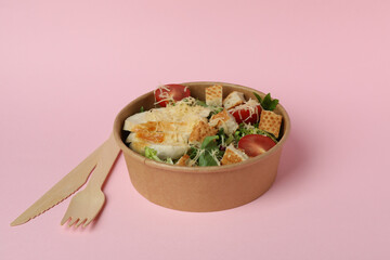 Bowl with Caesar salad and cutlery on pink background