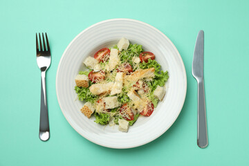 Plate with Caesar salad on mint background