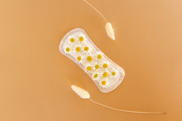 A sanitary pad with chamomile flowers on it lies on a yellow background. Menstruation days. Hygiene and freshness concept