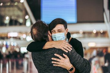  Woman in face mask welcoming her husband at airport