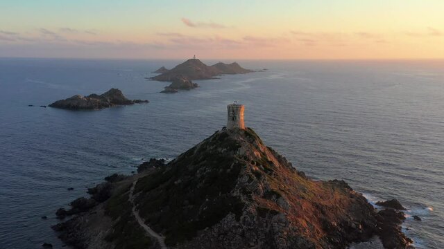Aerial view lighthouse on mountain rocky hill in sea sunset. Amazing footage of sunrise over the sea during colorful sunset, rocky island,lighthouse on the top of rocky seashore in sundown