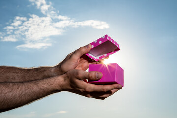 Male hand showing pink gift box with blue sky background. Valentines day concept. Small Handmade gift boxes in shiny blue night.