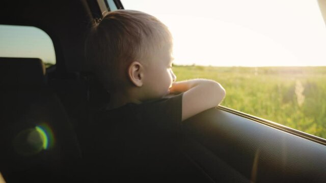 Happy family travel. Little boy leaning out of car window waving hand. Happy child putting her arm out of open window of a car. Summer road trip concept.