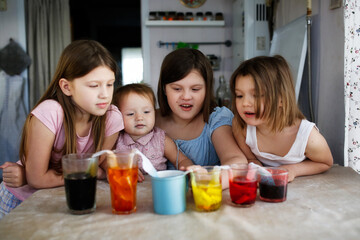 Home experiments with different colors, food dyes. Children play with colored water. Four children are experimenting with colorful drinks at the table.