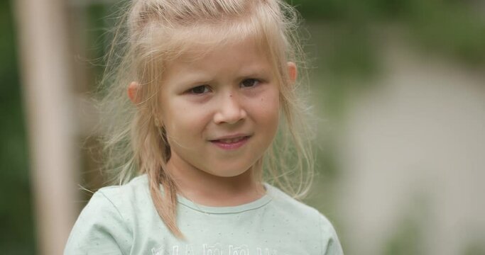 close up of beautiful little blonde girl standing outside in summer breeze, smiling and looking innocent while posing