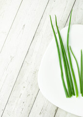 Fresh green onions on a white plate, wooden background. Diet food concept. Flat lay. Vertical photo.