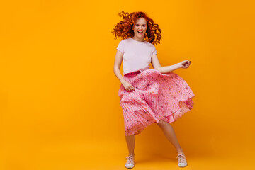 Young woman in midi skirt and cropped t-shirt jumping and dancing on orange background