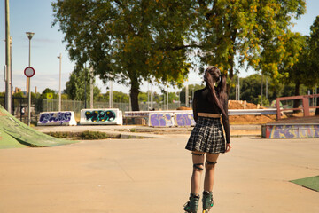 Young girl with punk style, pigtails and inline skates skating seen from the back.