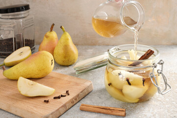 Pouring flavored sugar water in a glass jar with sliced pear, cinnamon and cloves on rustic stone,...