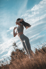 Fashion outdoor photo of beautiful woman with dark hair in luxurious sport dress posing in summer field.