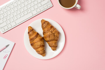 Above photo of keyboard cup of coffee notebook with pen paper clips and plate with two croissants isolated on the pink backdrop with blank space