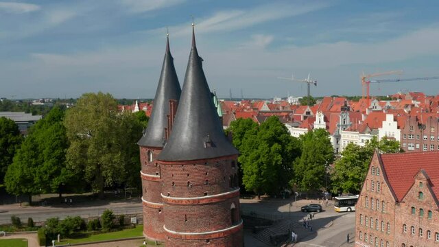 Aerial orbit shot around Holstentor, medieval town gate. Big church Marienkirche with two green towers in background. Luebeck, Schleswig-Holstein, Germany