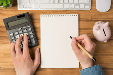 First person top view photo of female hands touching calculator and holding pen over organizer...
